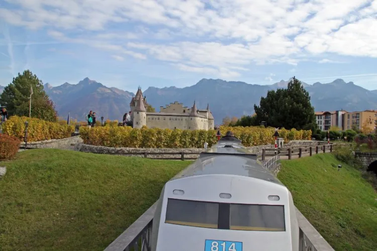 An Amtrak miniature train passing a small Chateau d'Aigle Castle in the Swiss Vapeur Parc